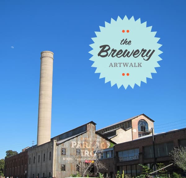 The Brewery Artwalk sign with an industrial building and chimney in the background.