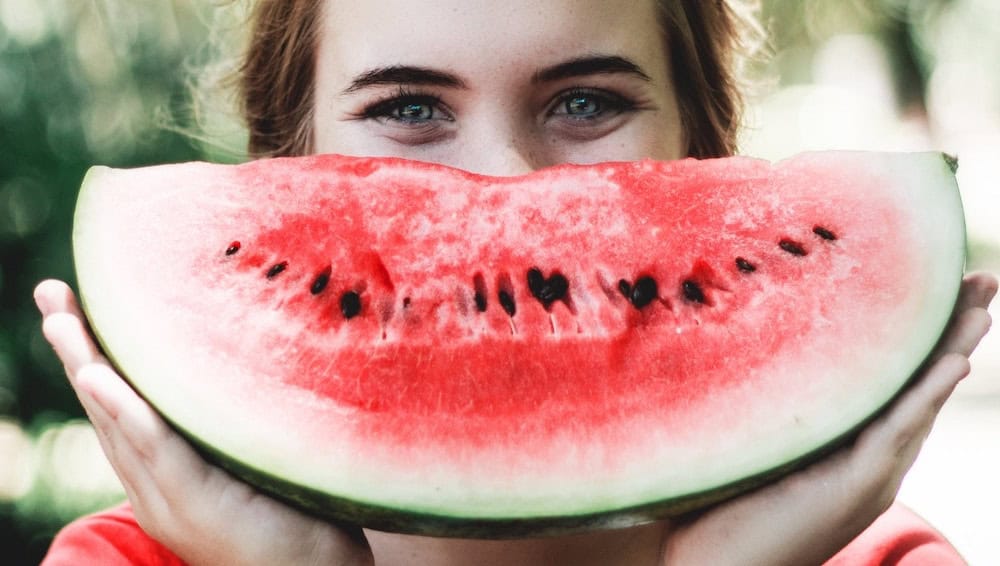 Young woman holding a large slice of watermelon in front of her face.