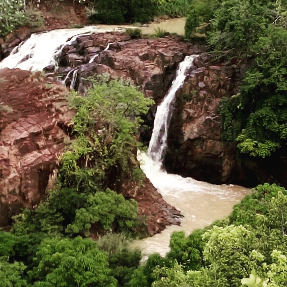 Scenic view of a waterfall cascading over red rocks surrounded by lush green trees.