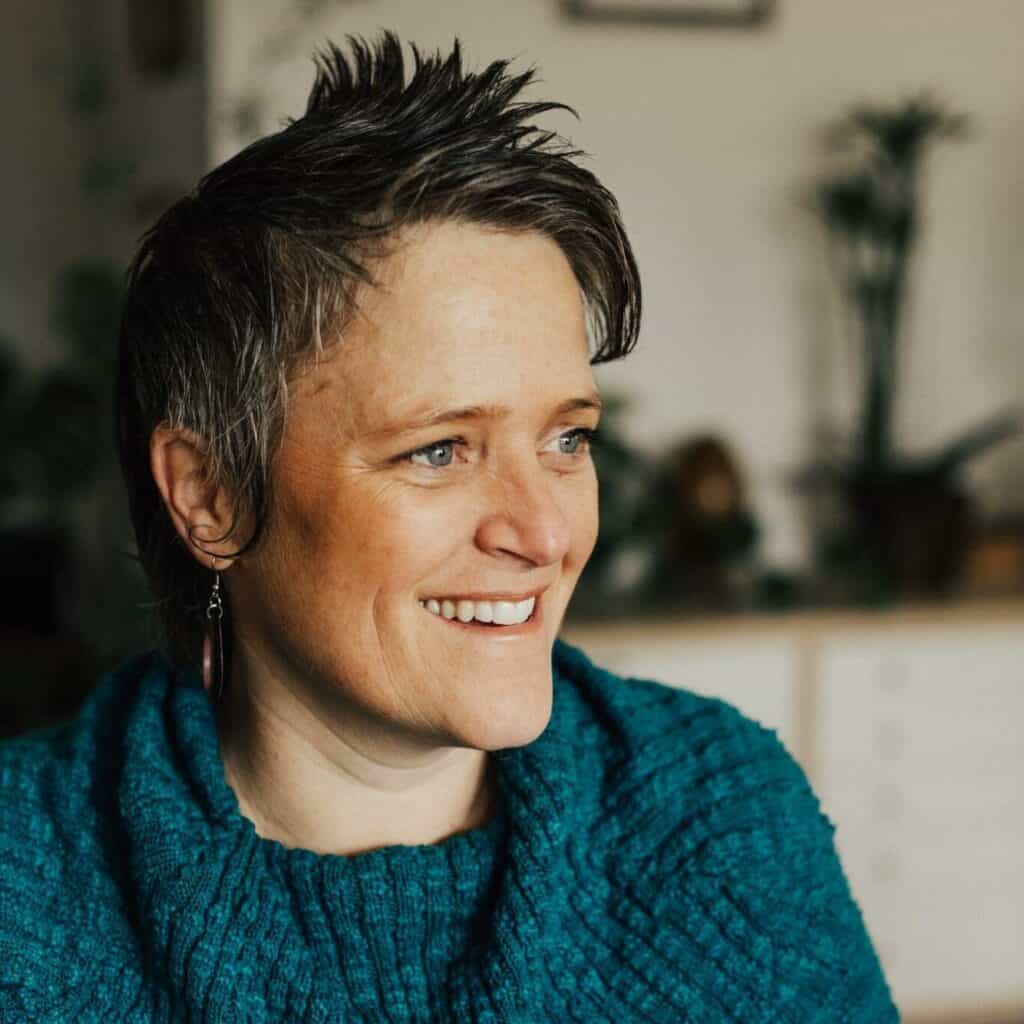 Smiling woman with short spiky hair wearing a blue sweater indoors.