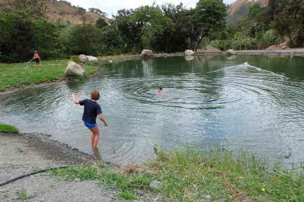 Children playing and swimming in a natural outdoor pond surrounded by trees.