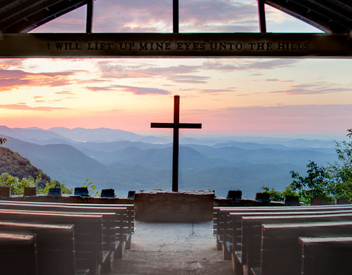 Scenic view of a cross at a mountain overlook during sunset with a quote above.