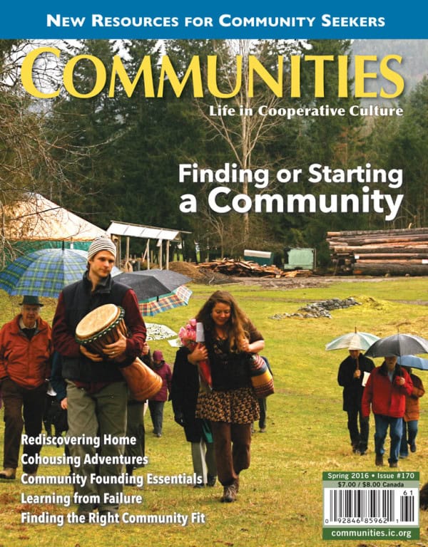 People gathering outdoors at a community event with tents and umbrellas.