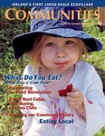 Young girl holding a red berry outdoors, wearing a blue hat and white shirt.