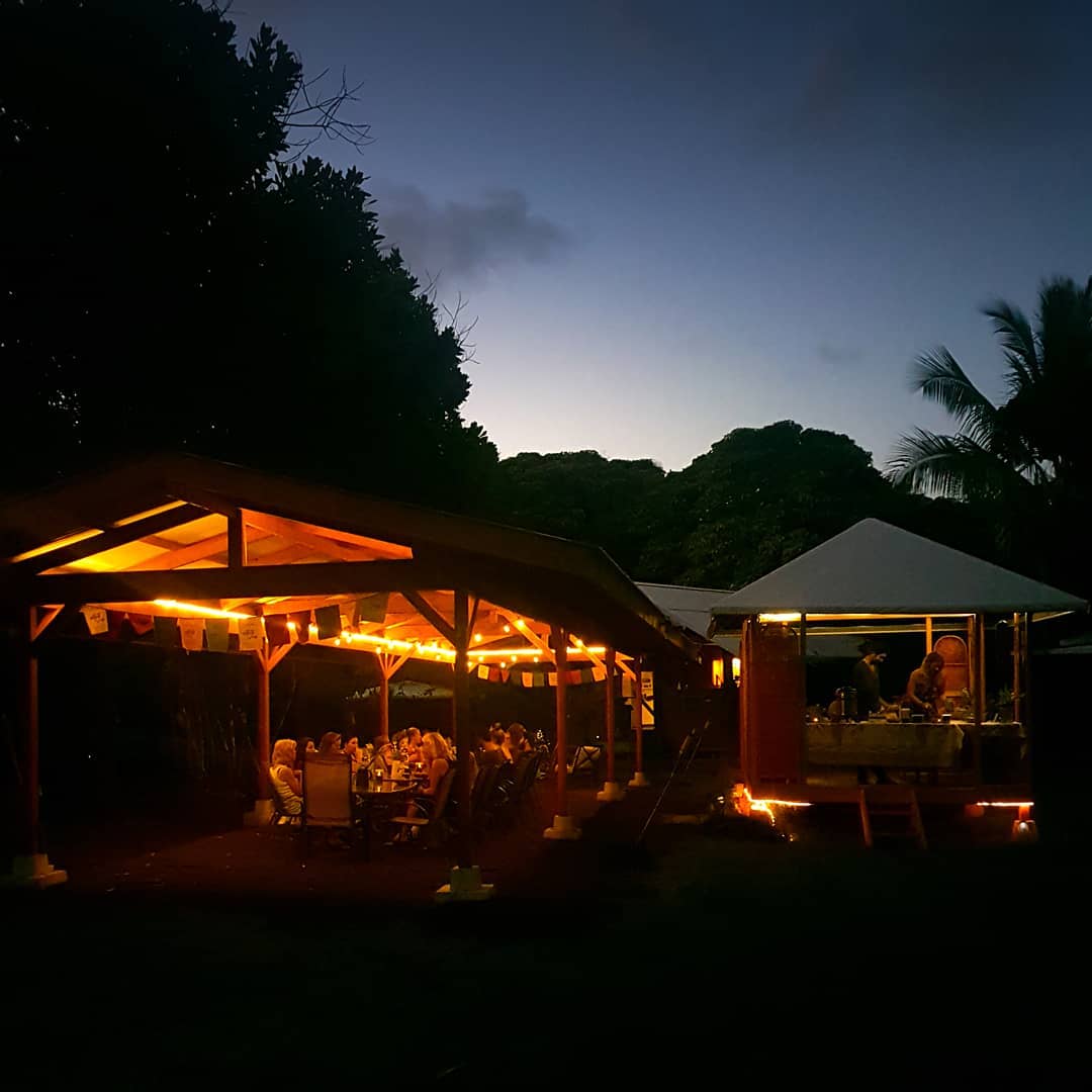 Outdoor community gathering at dusk with string lights and tents in Hawaii.