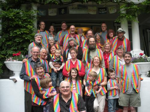 Group of diverse people wearing rainbow striped shirts outside a building.