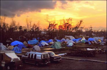 Sunset over a makeshift homeless encampment with tents and vehicles.