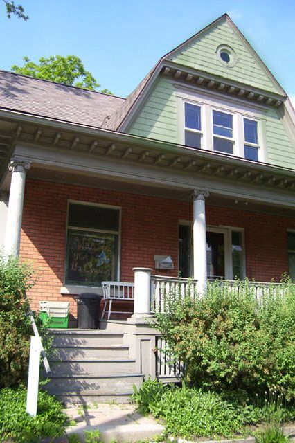 Historic house with green gable and brick facade, surrounded by lush greenery.