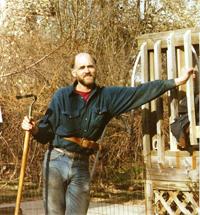 Man with a beard in casual clothing standing outdoors near a vehicle.