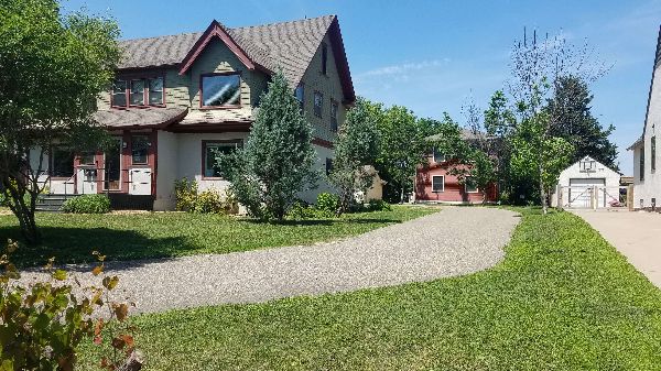 Charming residential house with lush green yard and trees under a clear blue sky.