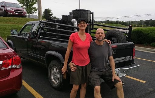 Two people smiling in front of a black pickup truck at a parking lot.