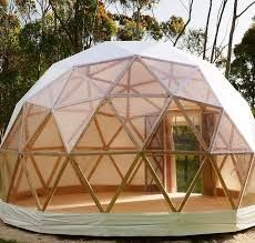 Geodesic dome structure with wooden framework and transparent panels in a natural setting.