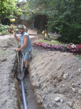 Worker installing underground piping in a garden trench for community infrastructure.