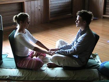 Two people sitting on a mat holding hands in a wooden room.
