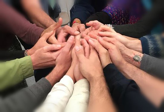 Group of diverse people joining hands in a circle for community teamwork.