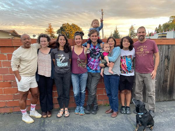 Diverse group of people standing outdoors in front of a brick wall at sunset.