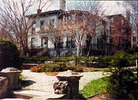 Historic residential building with lush garden and stone pathway in community setting.