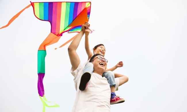Family flying a colorful rainbow kite outdoors on a clear day.