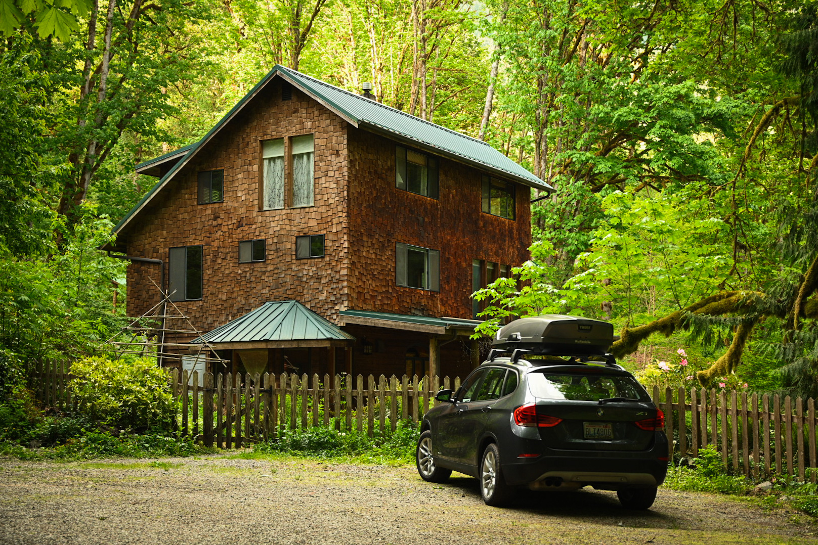Eco-friendly wooden house in lush forest with car parked outside.