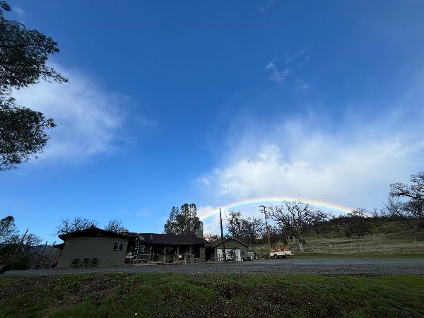 Scenic view of a rainbow over a rural landscape with a house and trees.