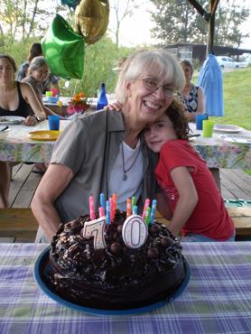 Elderly woman and young girl celebrating birthday outdoors with cake and balloons.