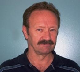 Portrait of a man with a mustache and short hair against a blue background.