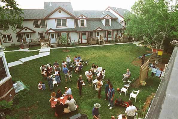 Community gathering in a lush green backyard with people socializing and children playing.