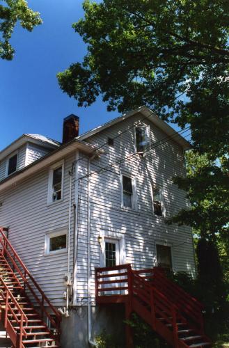 White multi-story house with red stairs and lush green trees in the background.