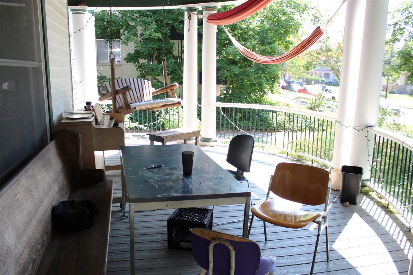 Cozy porch with hammock, chairs, and table overlooking a green yard.