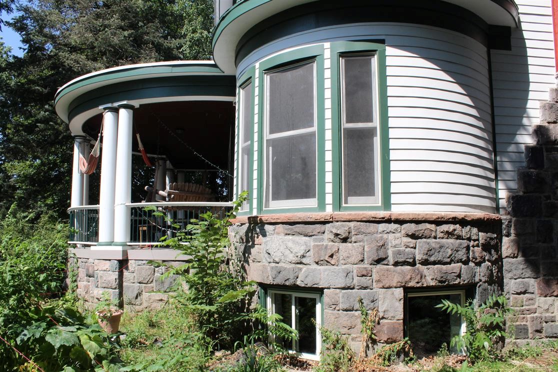 Historic house with rounded bay window and stone foundation in a lush garden.