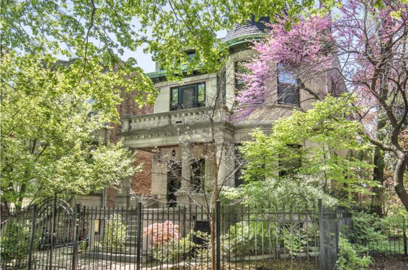 Historic house surrounded by lush green trees and pink flowering trees.