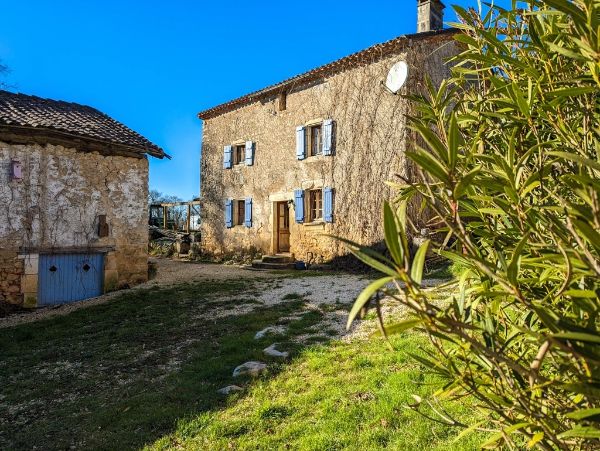 Rustic stone house with blue shutters in a rural setting under a clear blue sky.