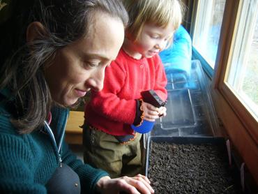 Woman and child planting seeds in a windowed indoor garden.