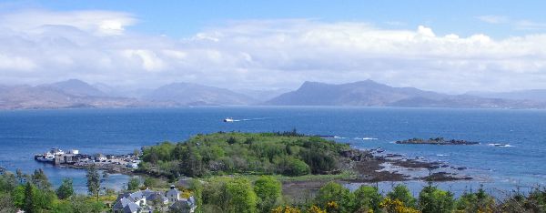 Scenic view of a small island with lush greenery in a blue sea, mountains in the background.