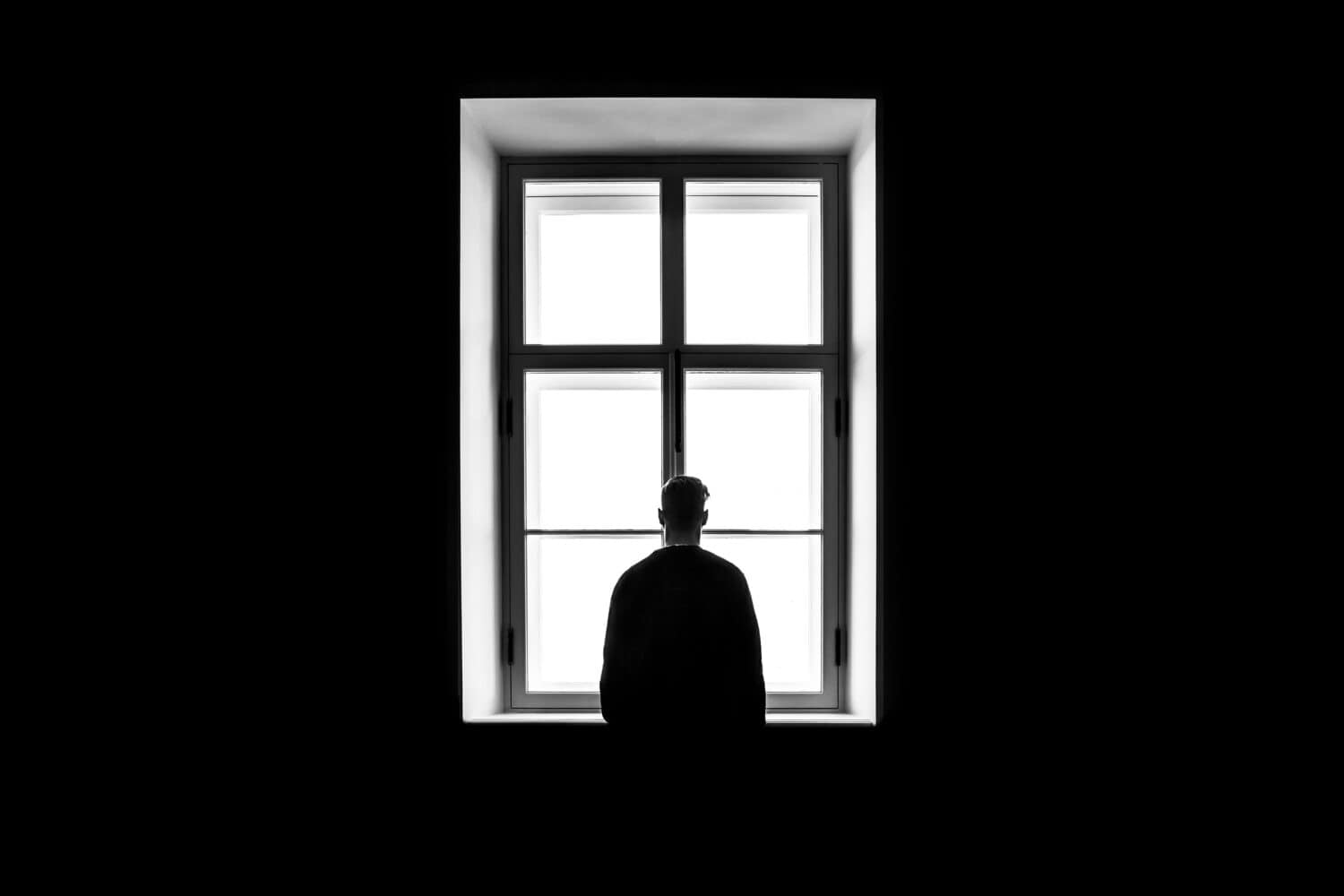 Person looking out a bright window in a dark room.