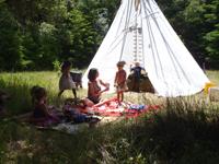 Children playing outside near a white teepee in a lush green setting.