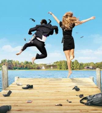 Two people jumping joyfully off a dock into a lake under a blue sky.