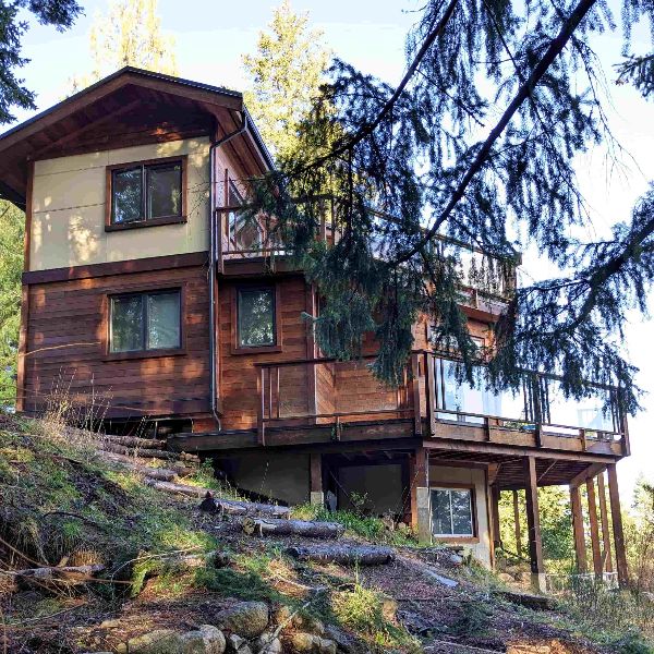 Wooden eco-friendly house on a hillside surrounded by trees.