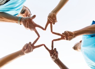 People forming a star shape with their hands in a community setting.