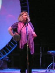 Woman singing on stage at a community event with a microphone and musical instruments.