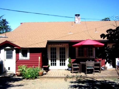 Red house with a deck, outdoor furniture, and a pink umbrella under a clear blue sky.