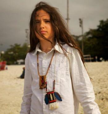 Young woman with long hair wearing a white shirt and necklace at the beach.