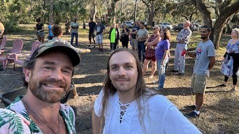 Group gathering at outdoor community event in a wooded area.