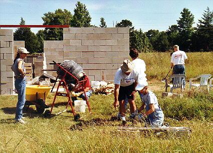 Community members building a brick wall outdoors at a construction site.