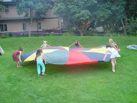 Children playing with a colorful parachute in a grassy yard.