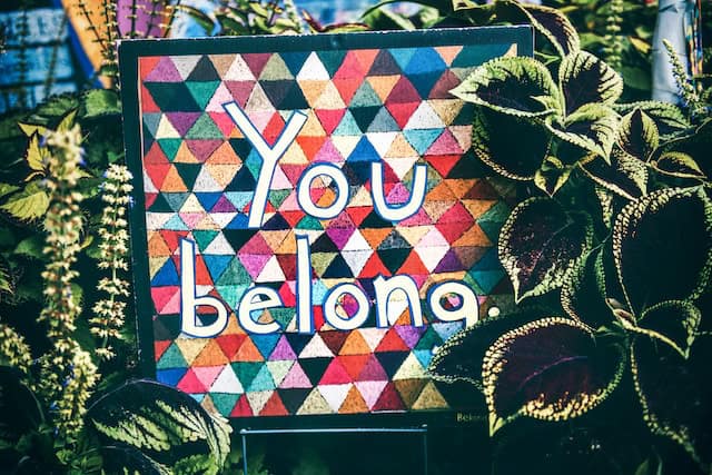 Colorful geometric patterned sign with 'You belong' message among green plants.