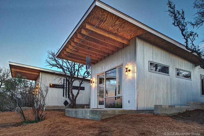 Modern tiny house with metal siding and large windows in a natural setting.