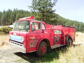 Vintage red fire truck parked in a grassy field with trees in the background.