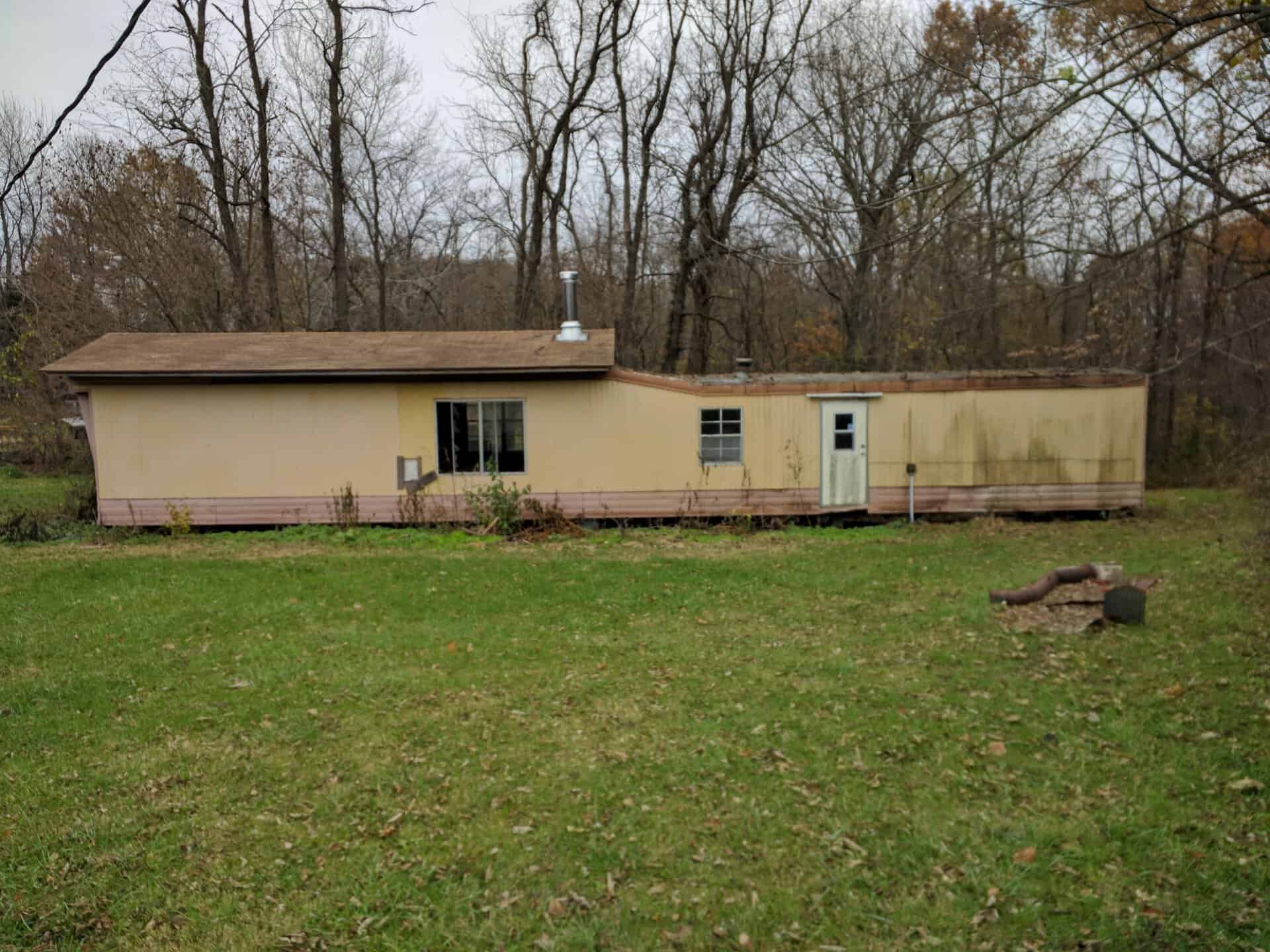 Single-story beige house with a flat roof in a wooded area.