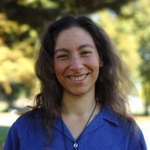 Smiling woman with long brown hair outdoors in natural light.